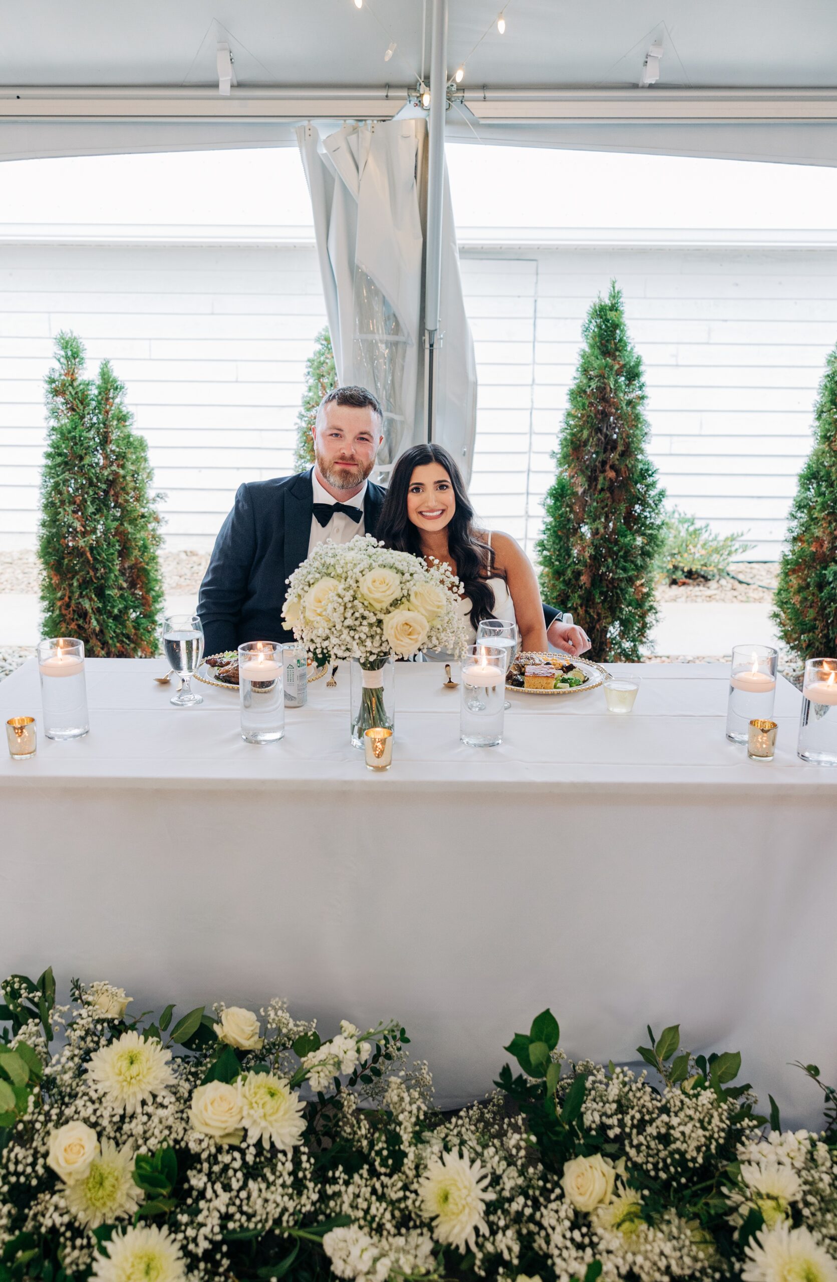 A bride and groom smile behind their head table covered in flowers at covington gardens