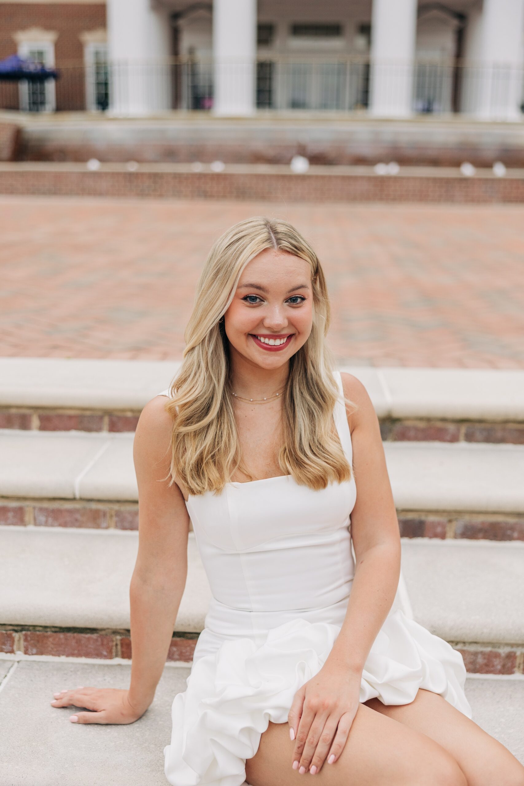 An image from a high point university graduation photographer of a woman in a white dress sitting on stairs outside