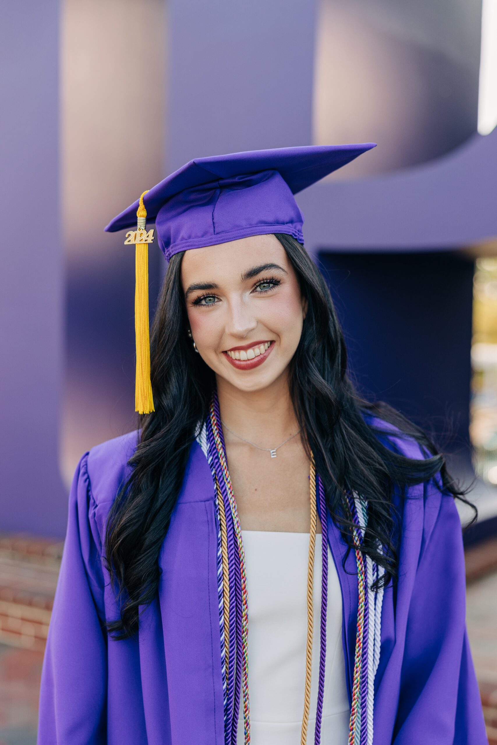 A happy grad in her purple cap and robe in front of the sign for an high point university graduation photographer