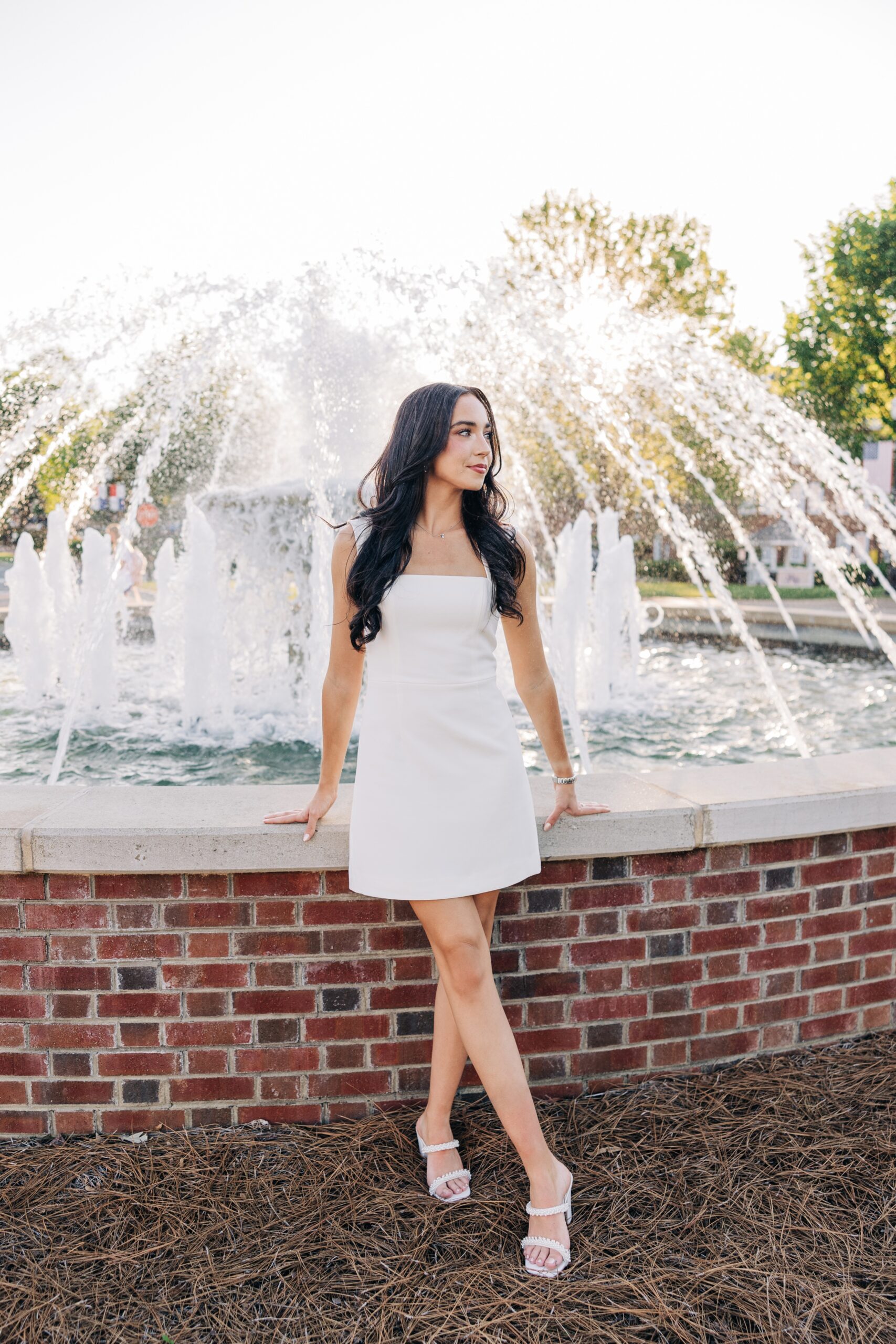 An image from a high point university graduation photographer of a woman in a white dress leaning on a fountain