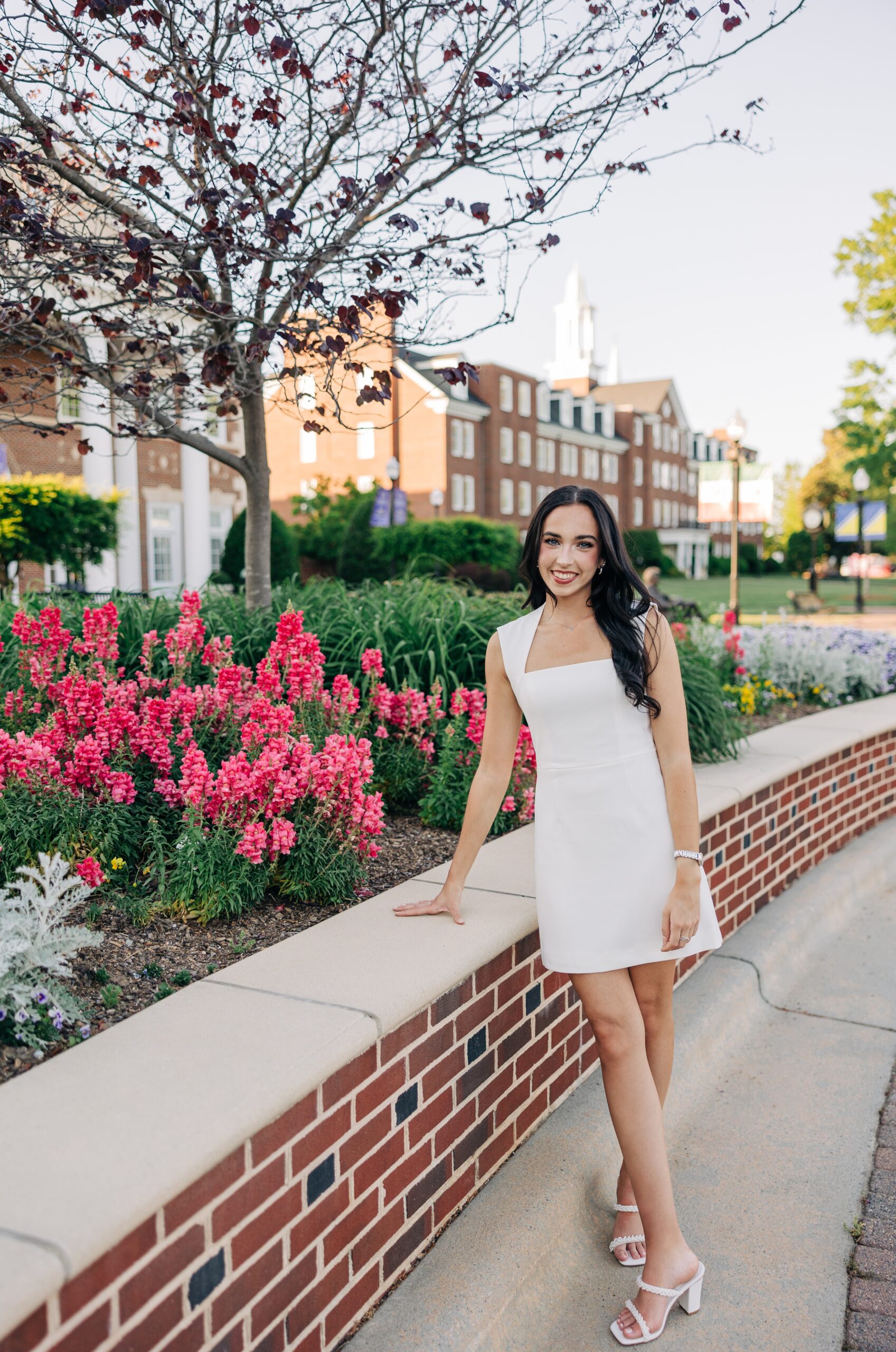 A high point university graduation photographer image leaning on a garden planter in a white dress