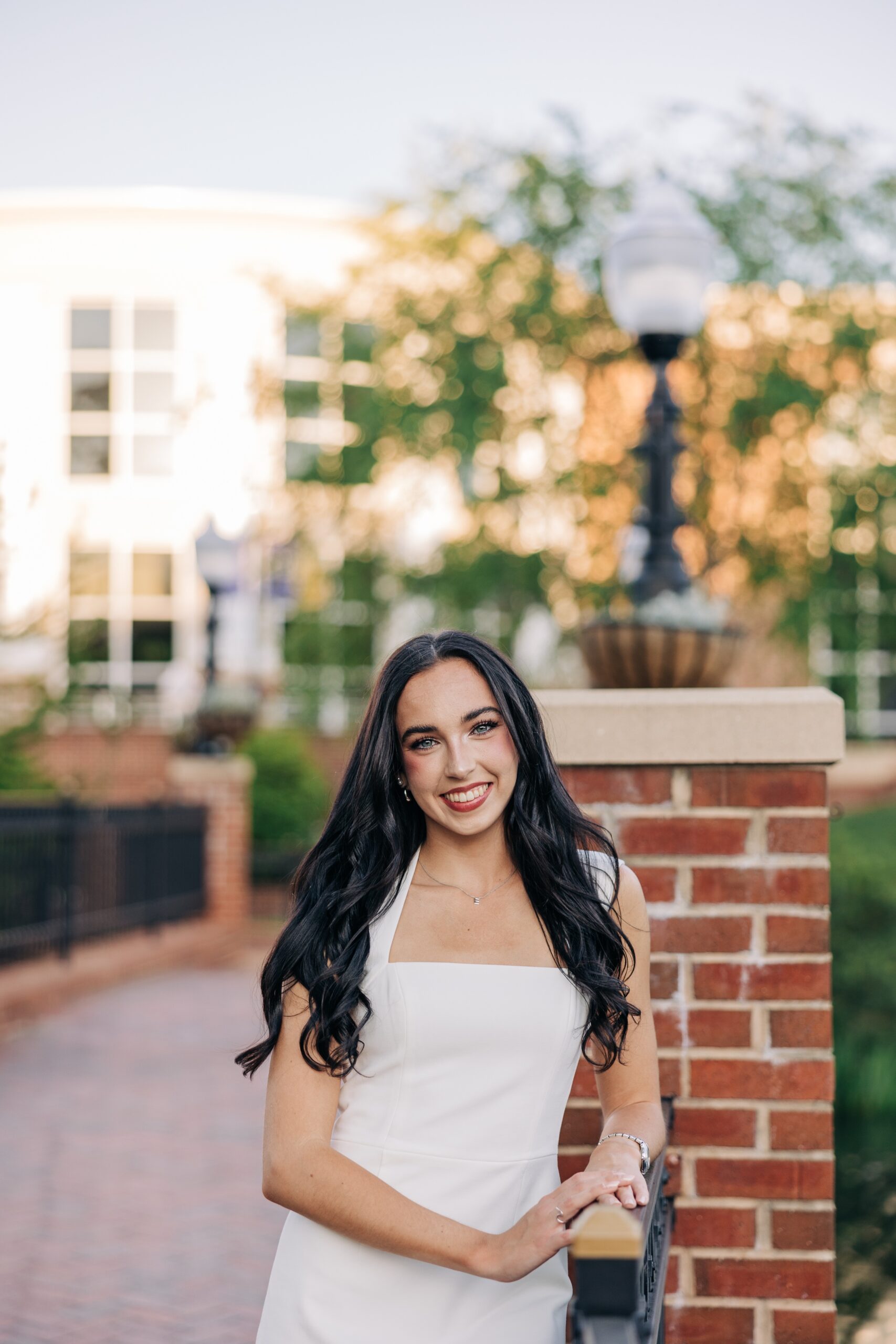 An image from a high point university graduation photographer of a grad in a white dress leaning on an iron fence