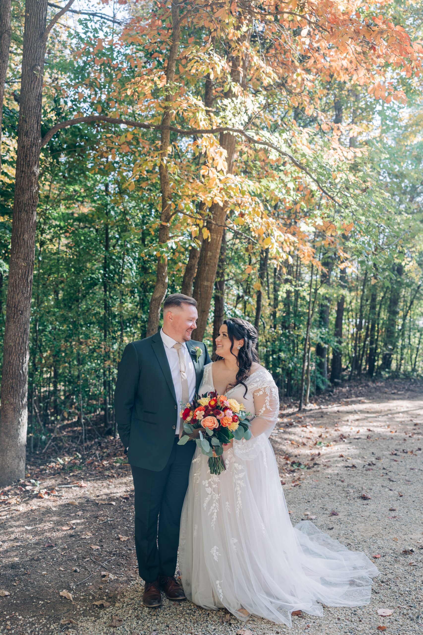 Newlyweds smile at each other while walking in the forest with large colorful bouquet