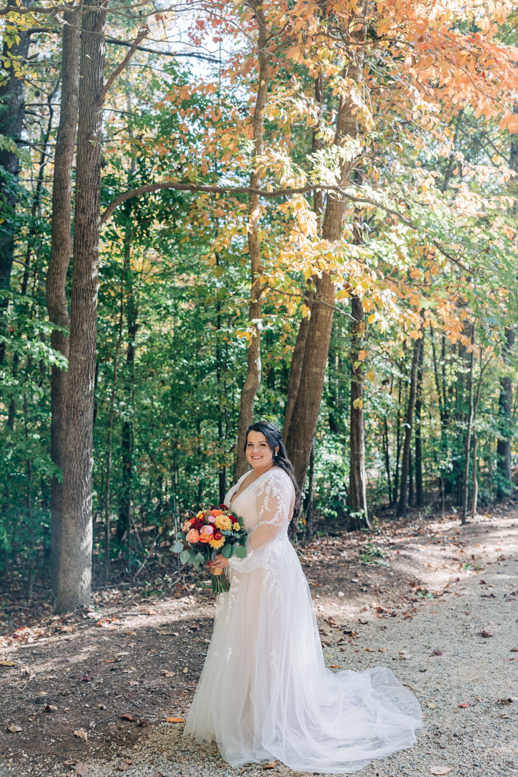 A bride smiles while holding her colorful bouquet in a forest