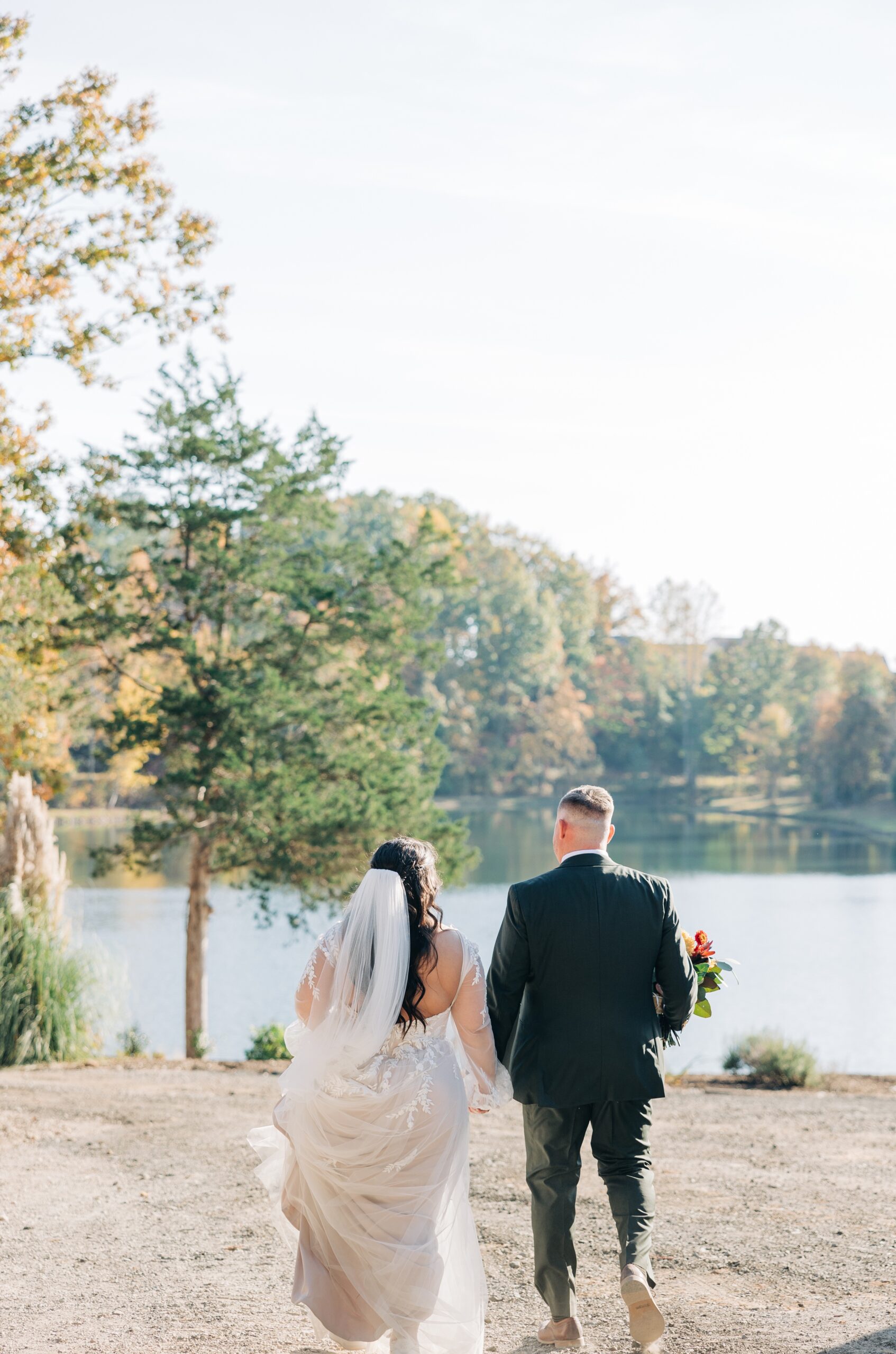 A brie and groom walk towards the pond holding hands at sunset