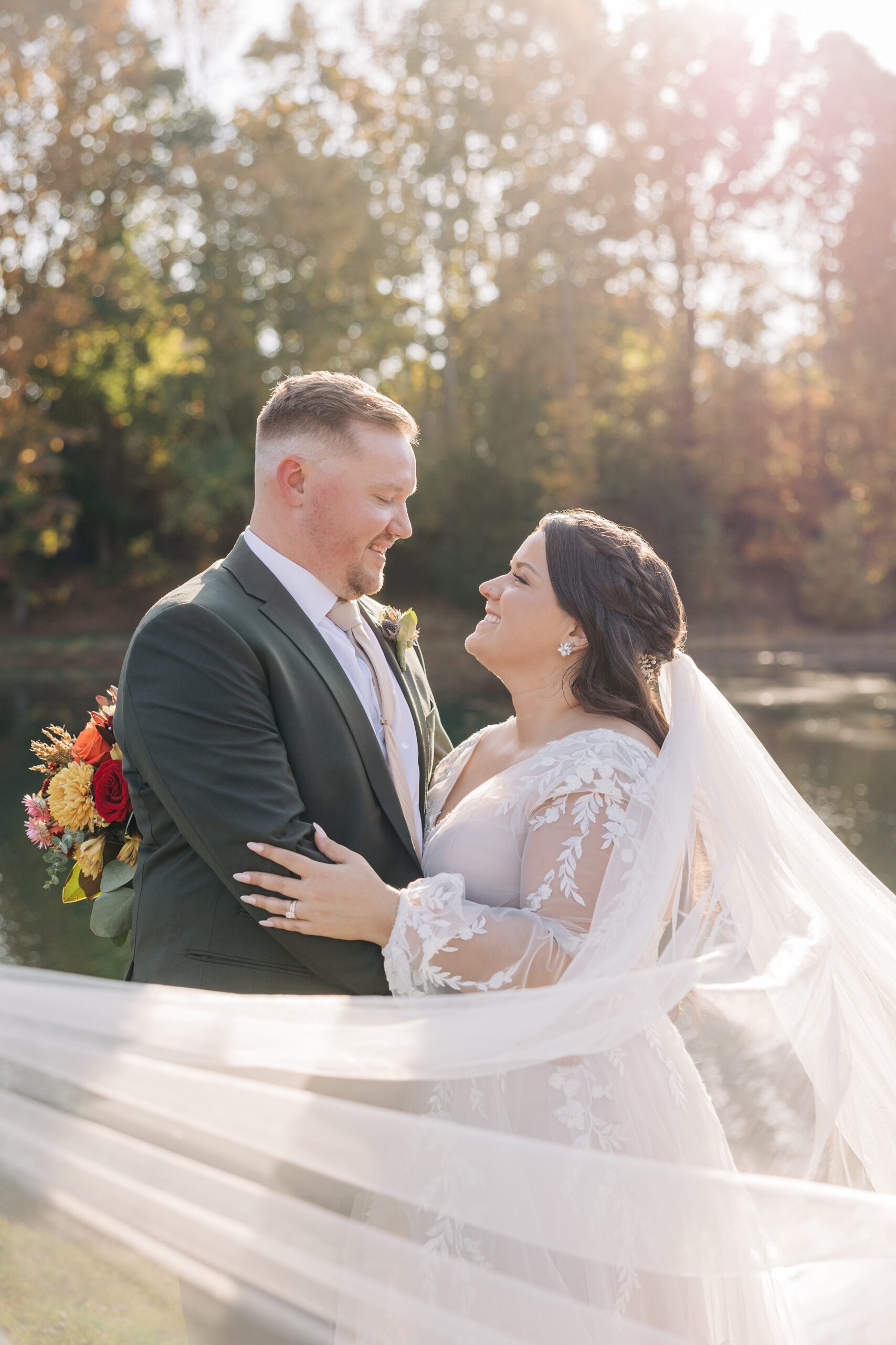 Newlyweds smile at each other while hugging at sunset by the water