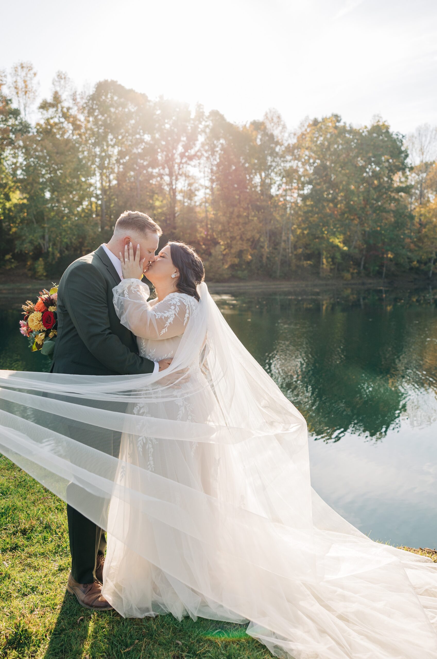 Newlyweds kiss on the edge of the water at sunset with the veil wrapped around them at splendor pond flower farm