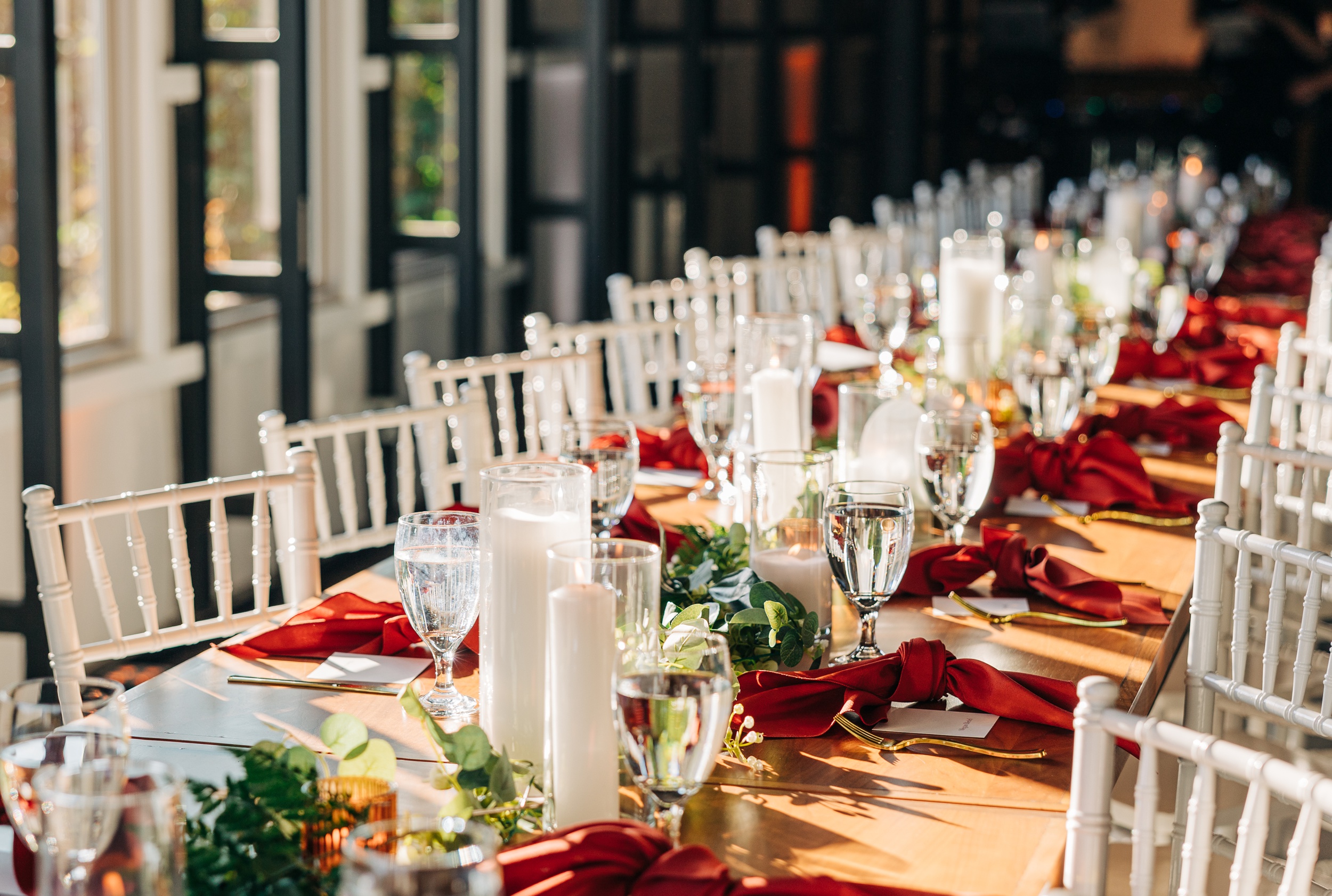 Details of a long wedding reception table set up with candles and red napkins at splendor pond flower farm