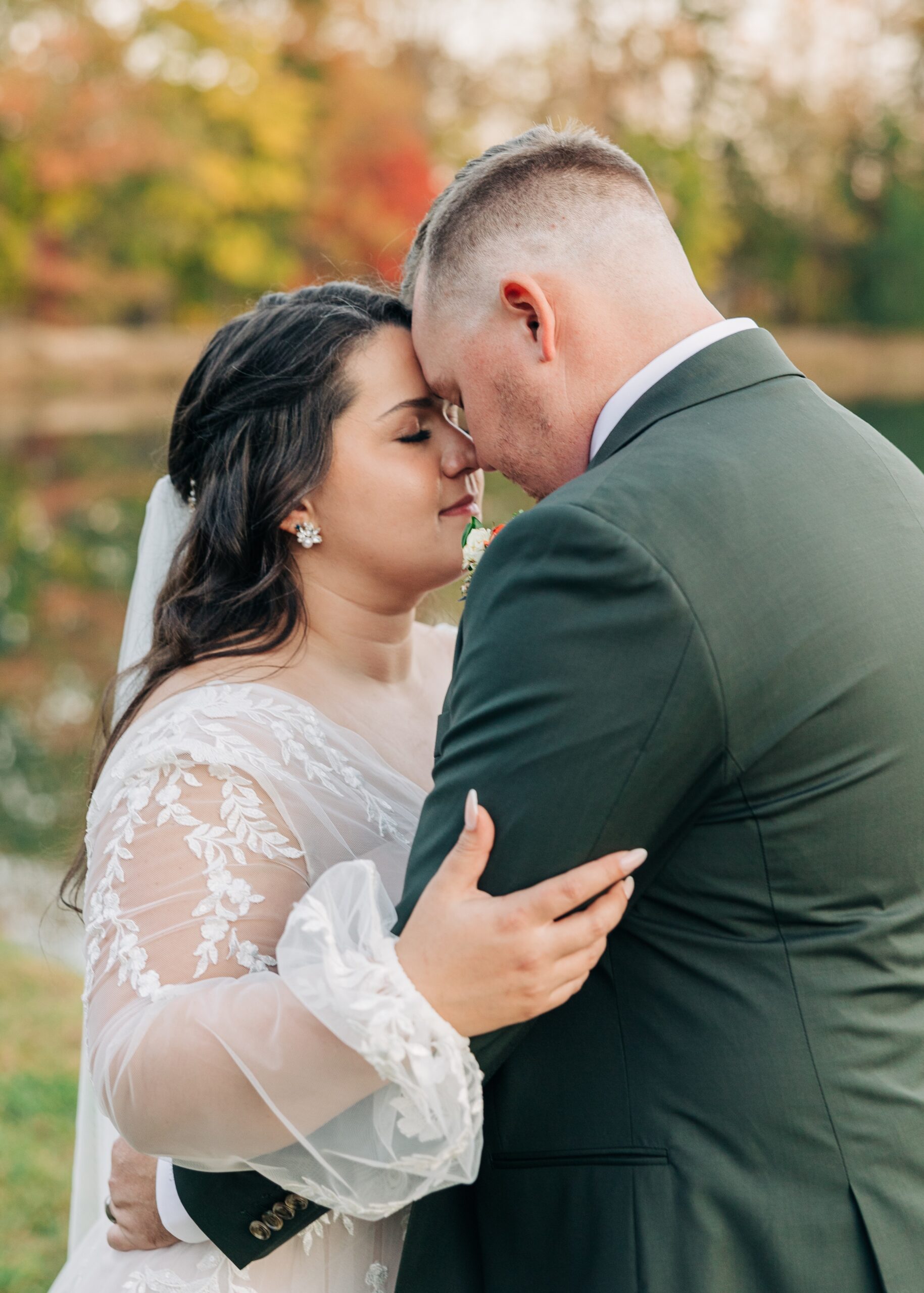 Newlyweds share a quiet moment by the water in fall touching foreheads