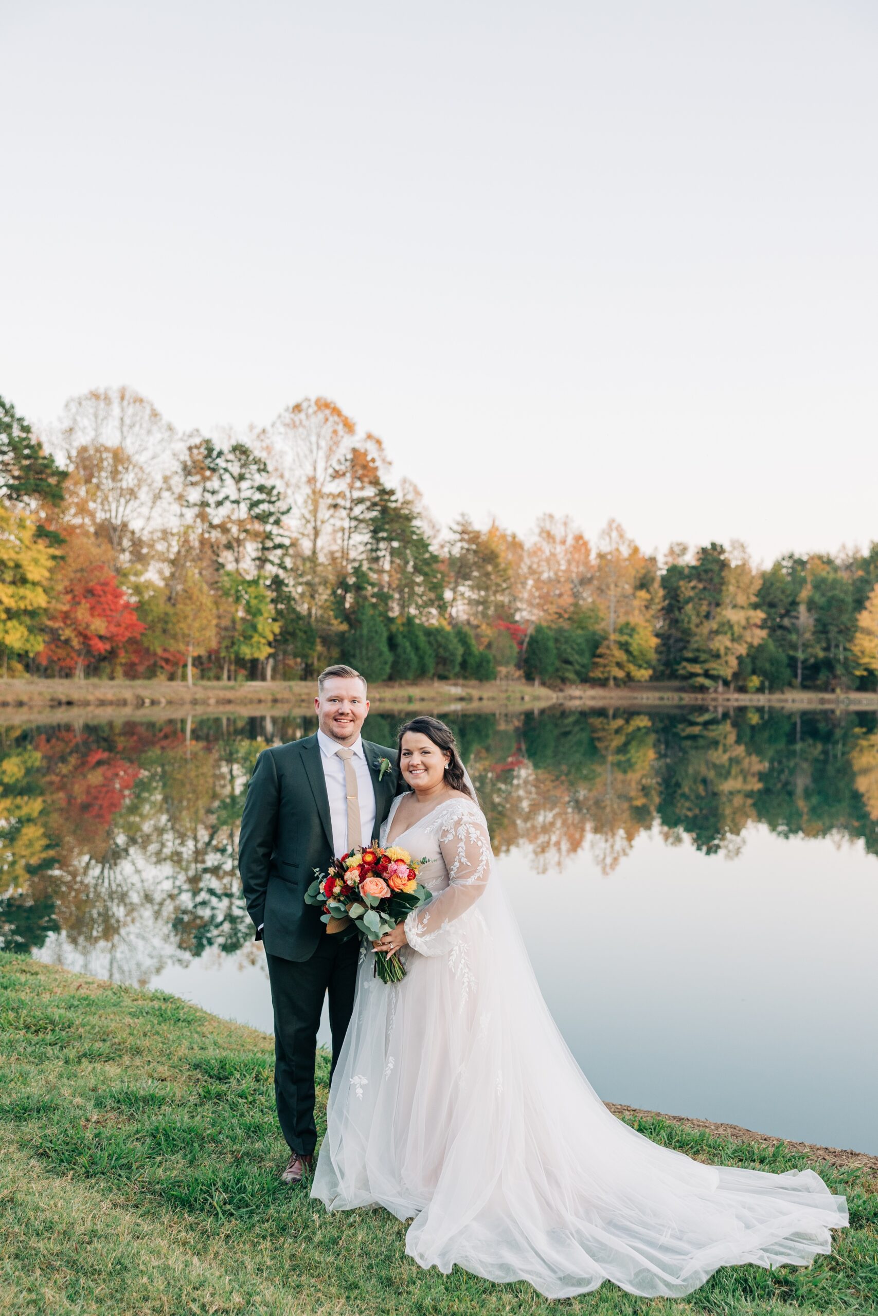 Happy newlyweds stand and smile together on the edge of the water at the splendor pond flower farm