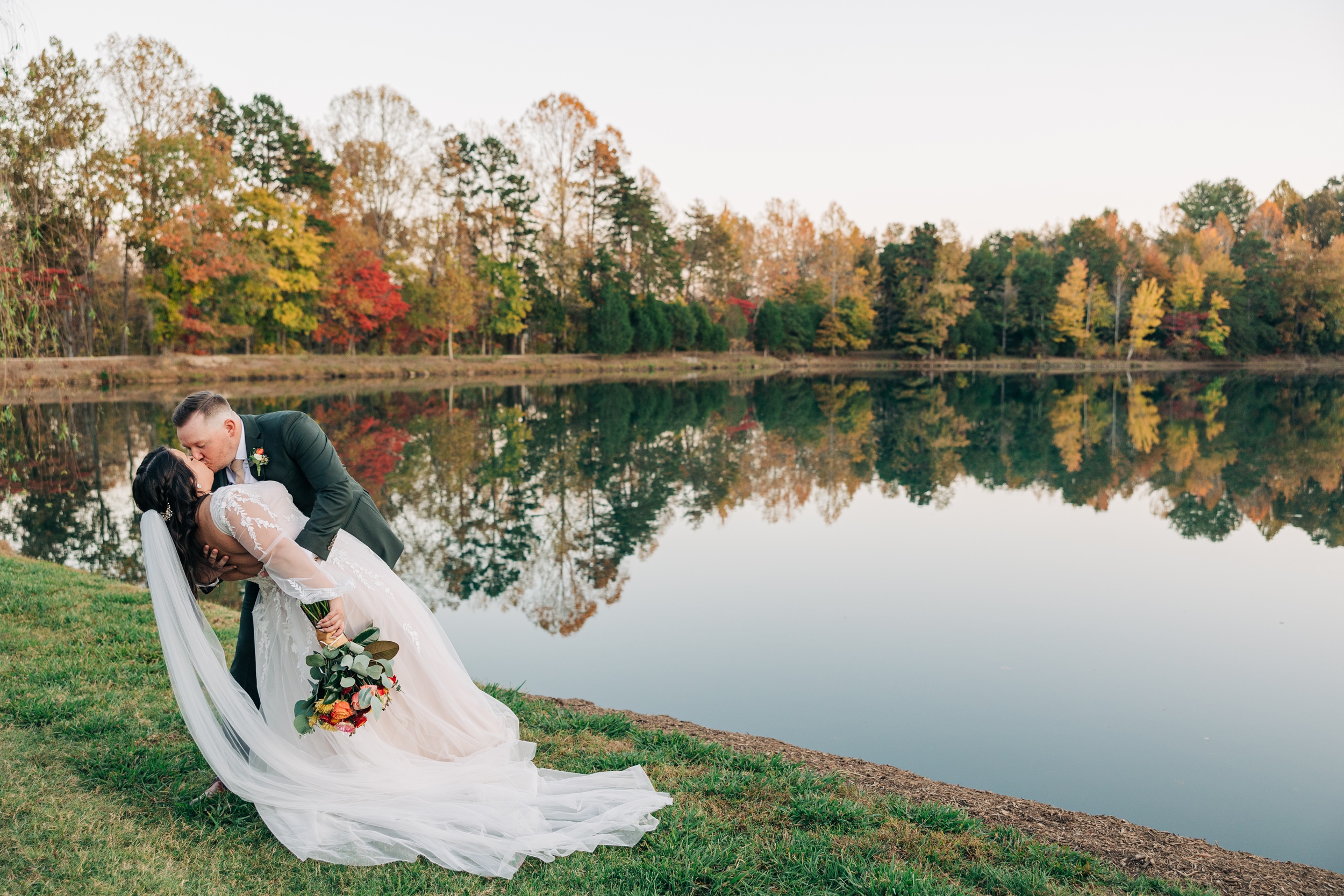 Happy newlyweds dip for a kiss by the water in fall at the splendor pond flower farm