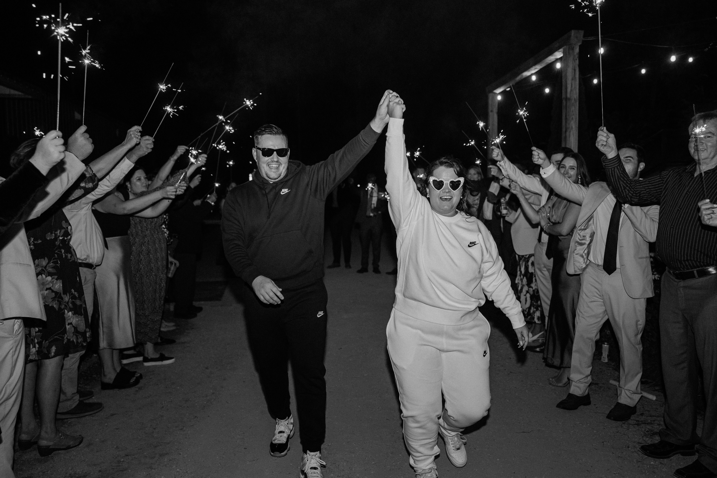 Happy newlyweds in sweat pants celebrate walking under sparklers to exit their wedding