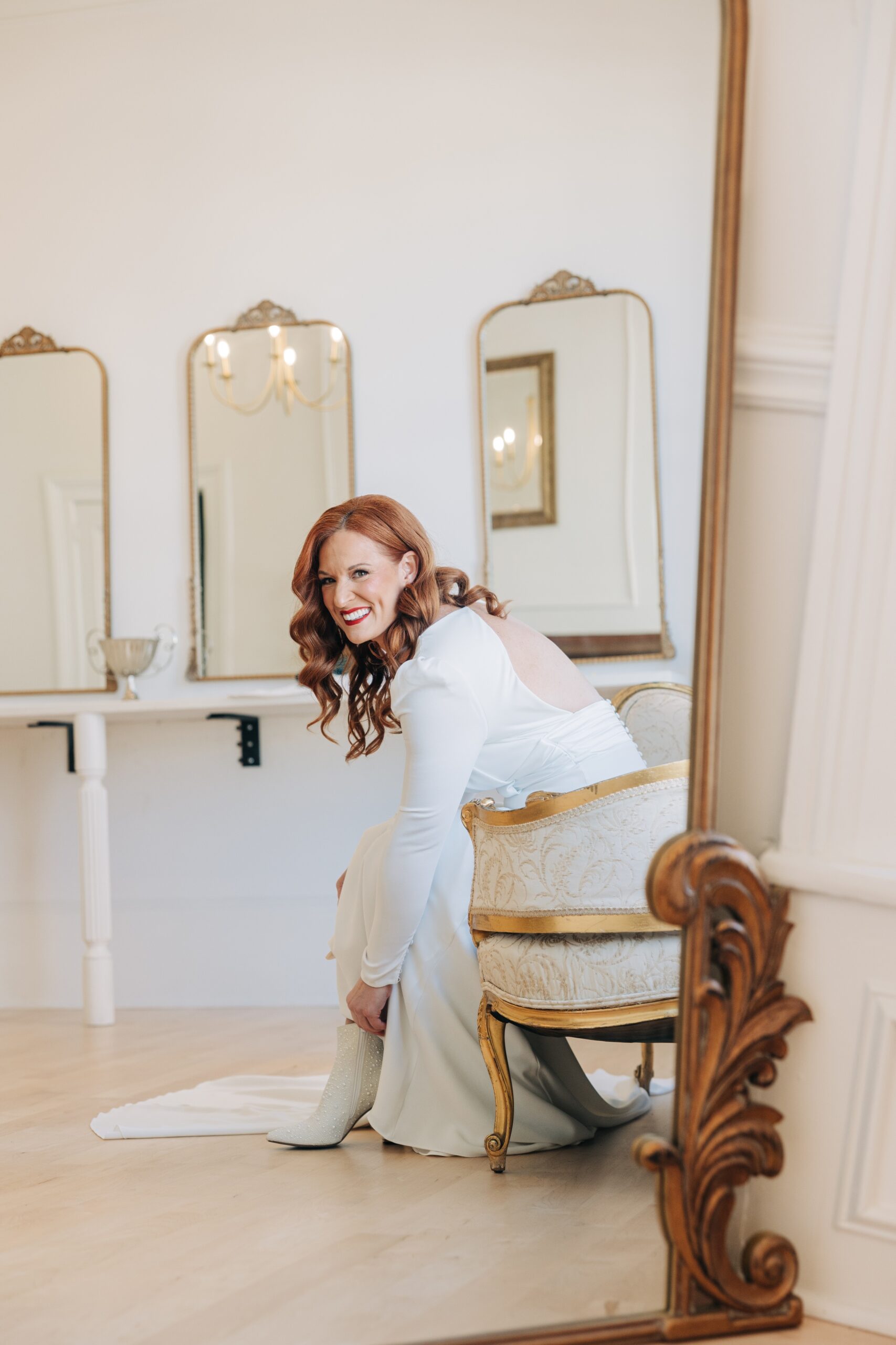 A bride laughs while putting on her shoes in a vintage chair at the crest winston-salem