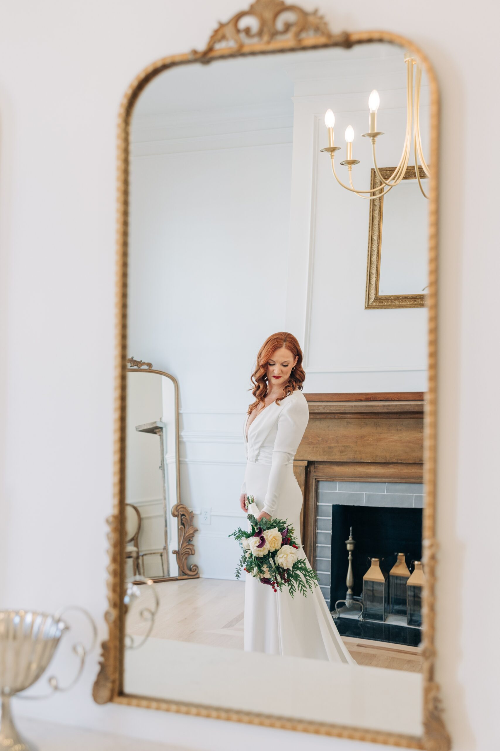 A bride gazes down her shoulder while standing in a mirror in her gown while getting ready at the crest winston-salem