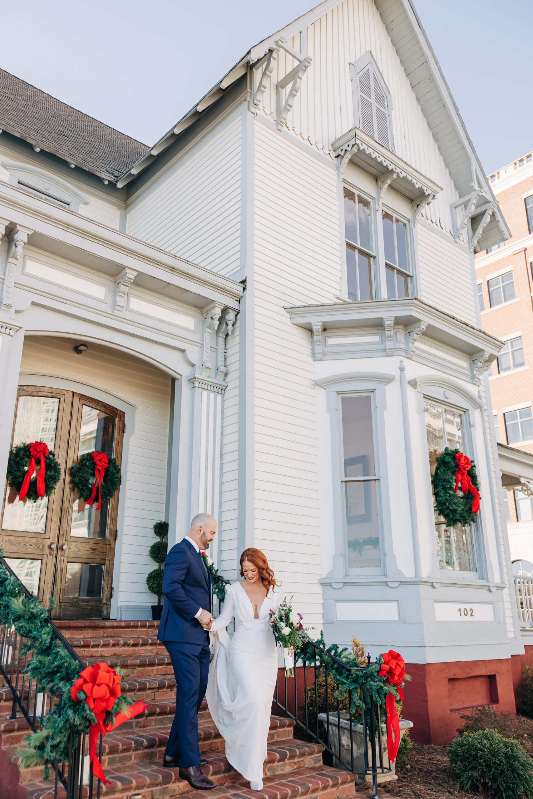 A groom in a blue suit helps his bride down the front steps of the crest winston-salem