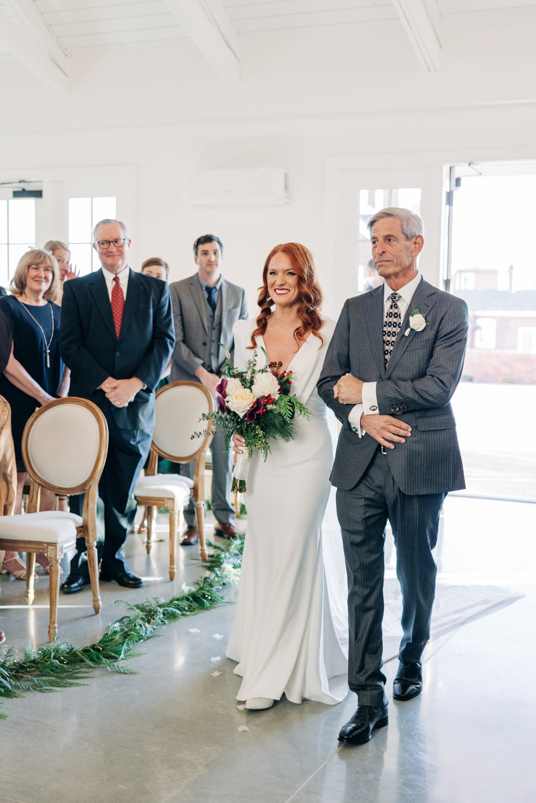 A bride walks down the aisle with her father in a grey suit