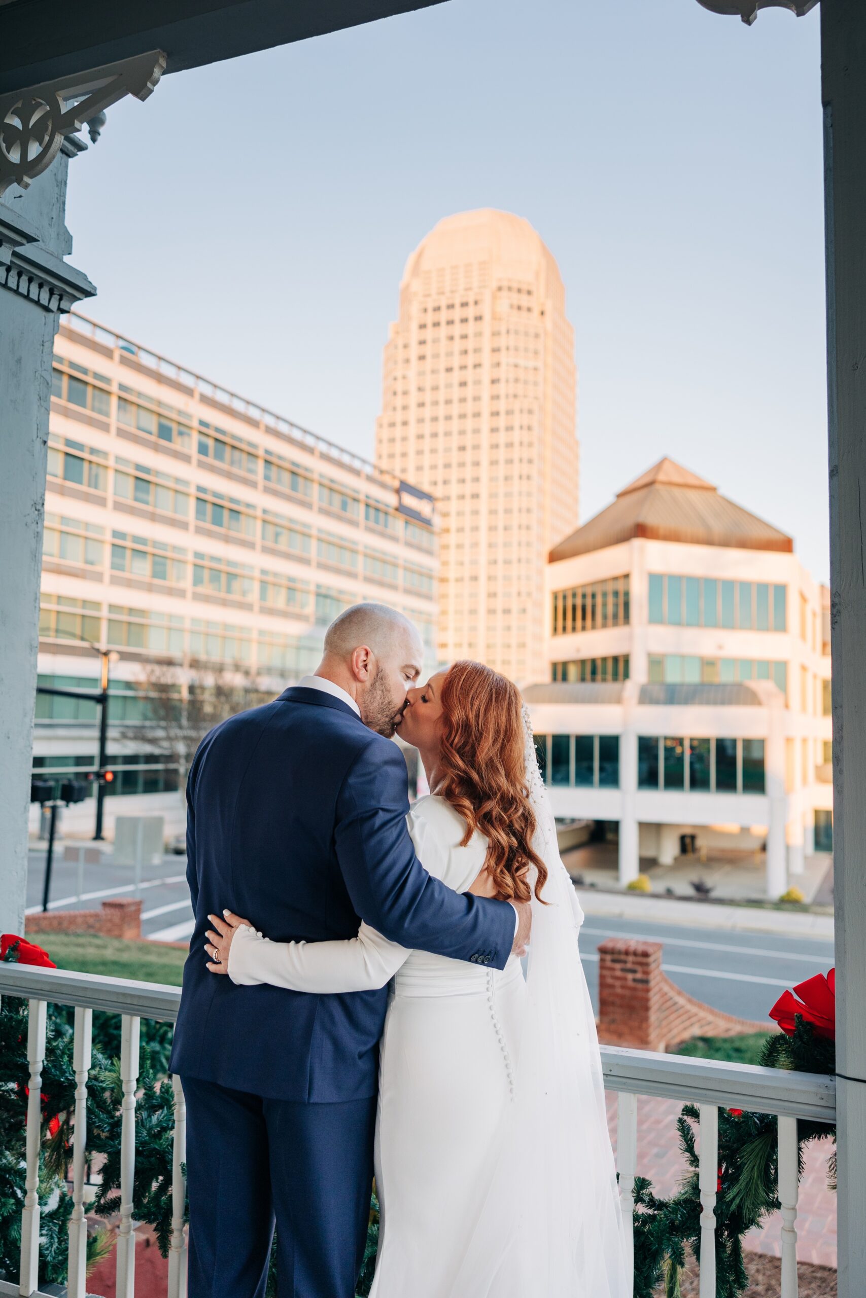 Newlyweds kiss on the porch of the crest winston-salem at sunset with skyline