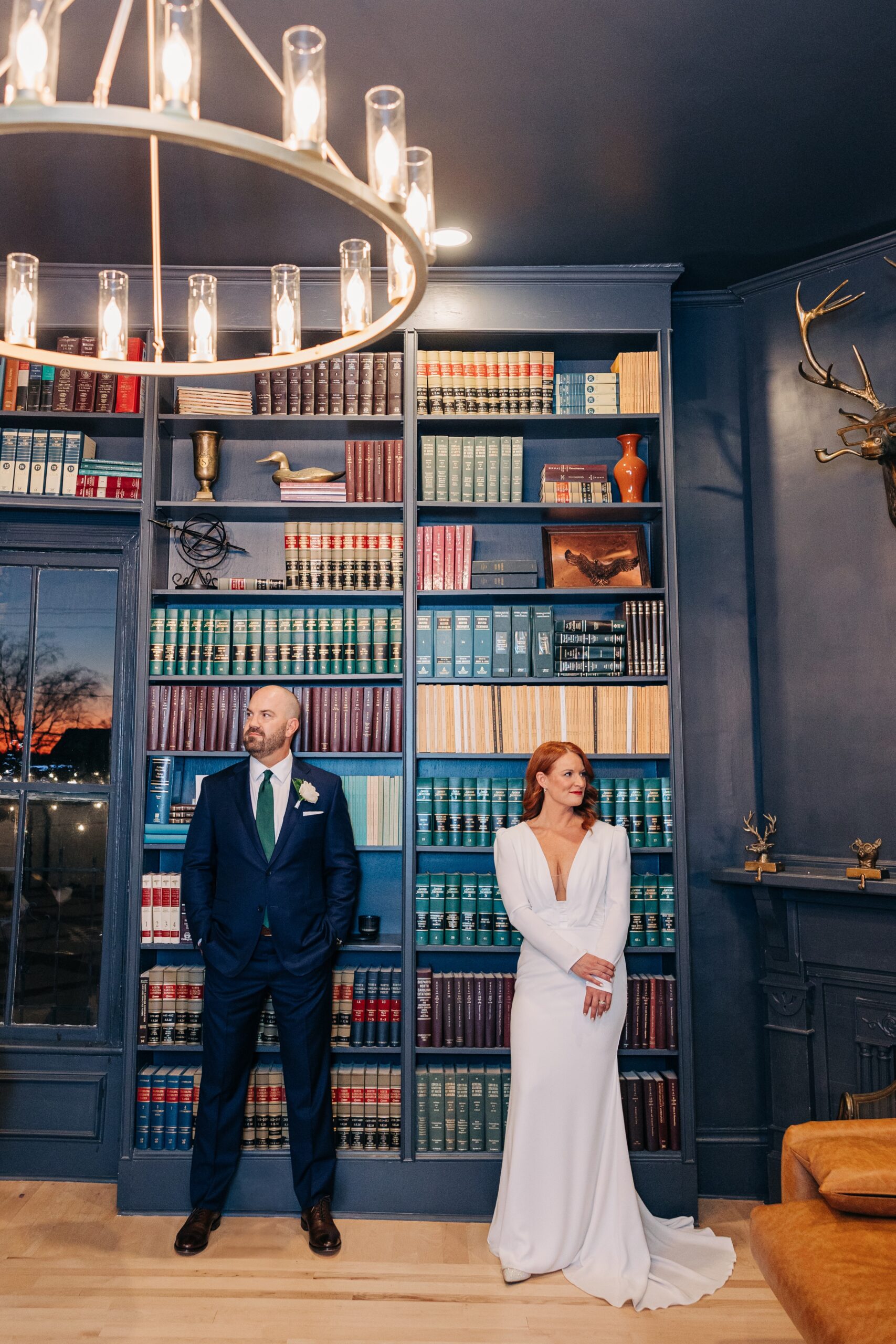 A bride and groom stand against a built in book case during their wedding at the crest winston-salem