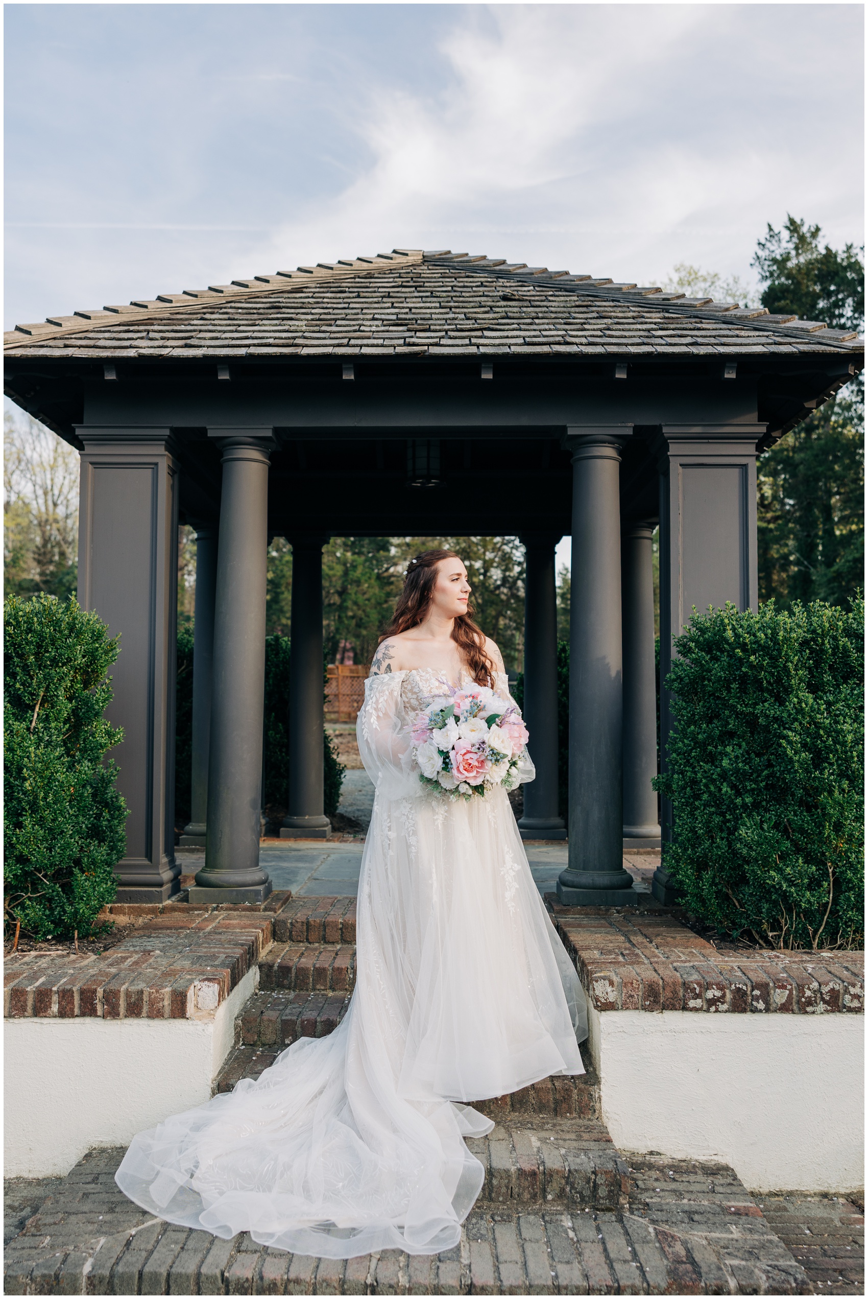 A happy bride smiles to the sunset while standing on brick steps holding her white and pink bouquet