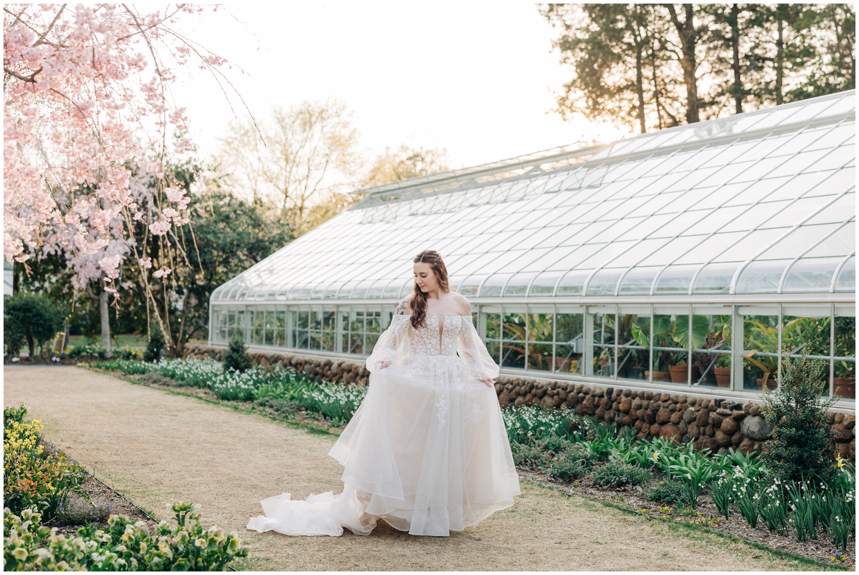 A bride admires her dress while walking through some stunning gardens and holding her train