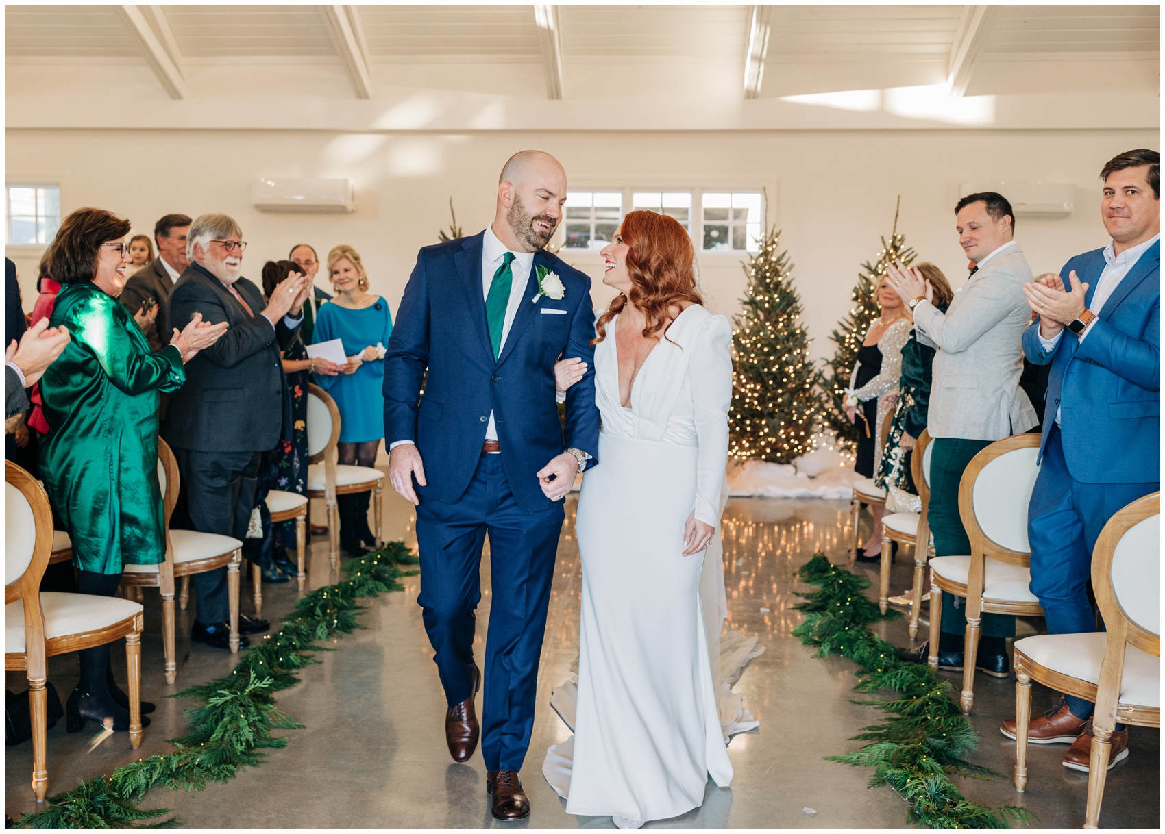 Newlyweds smile at each other while walking back up the aisle at the end of their christmas themed wedding ceremony