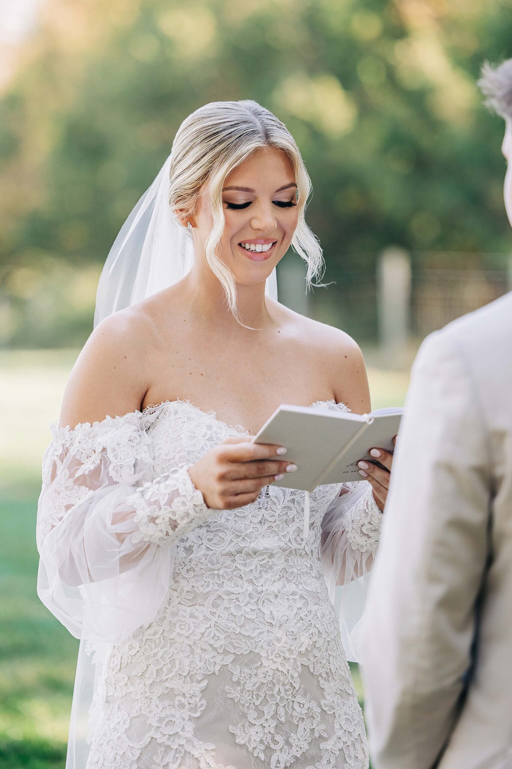 A bride smiles while reading a note to her groom during their first look in a lace gown