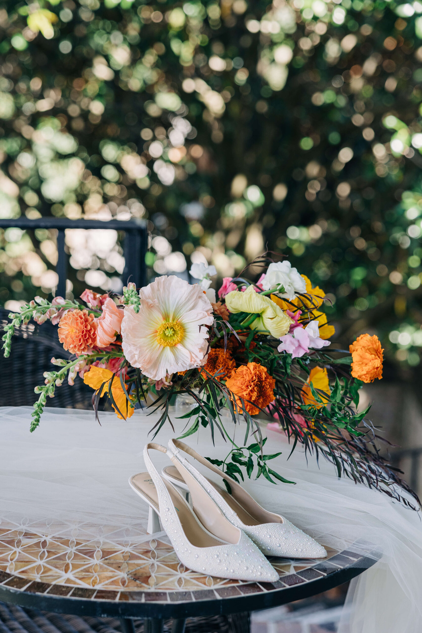 Details of a bride's shoes, veil and bouquet on a garden patio table