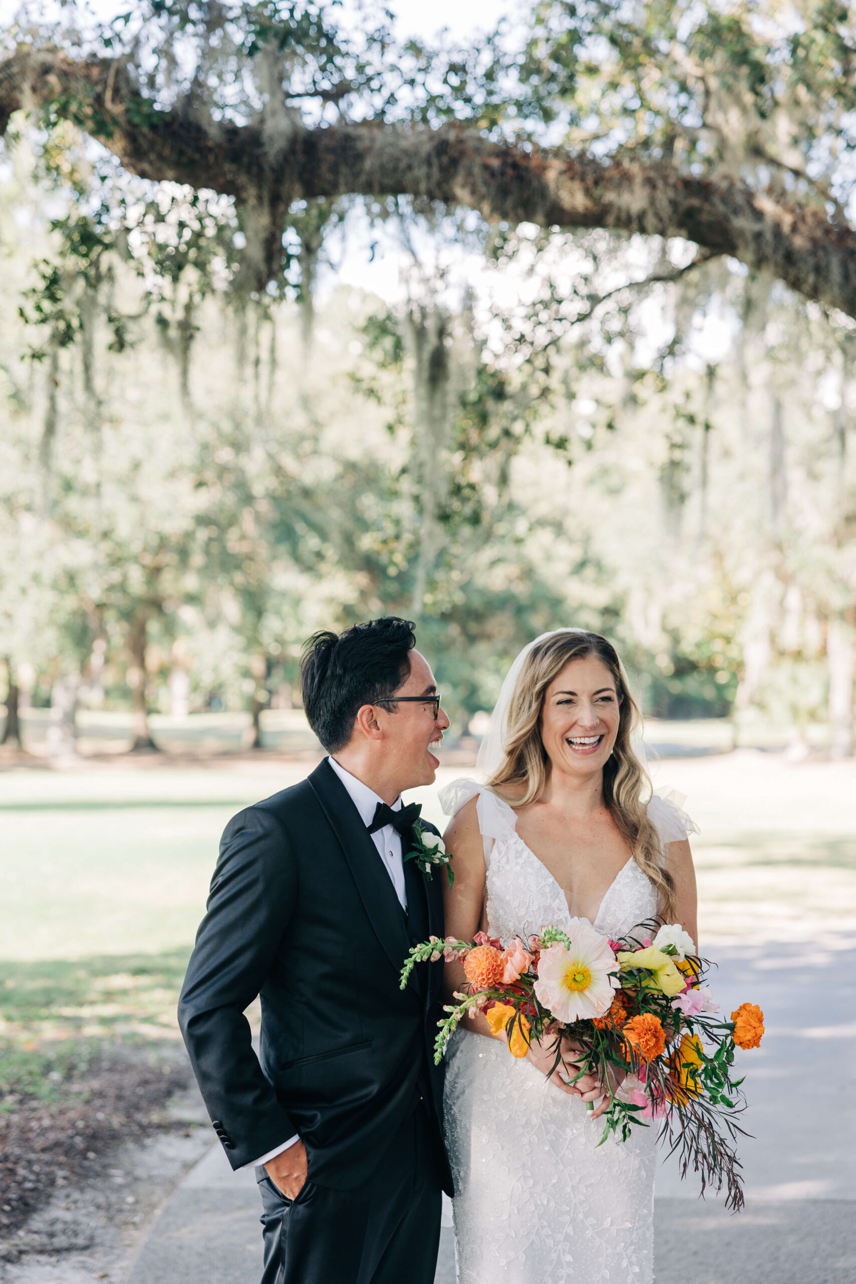 Newlyweds laugh in a sidewalk under live oaks during their Dunes West Golf Club wedding