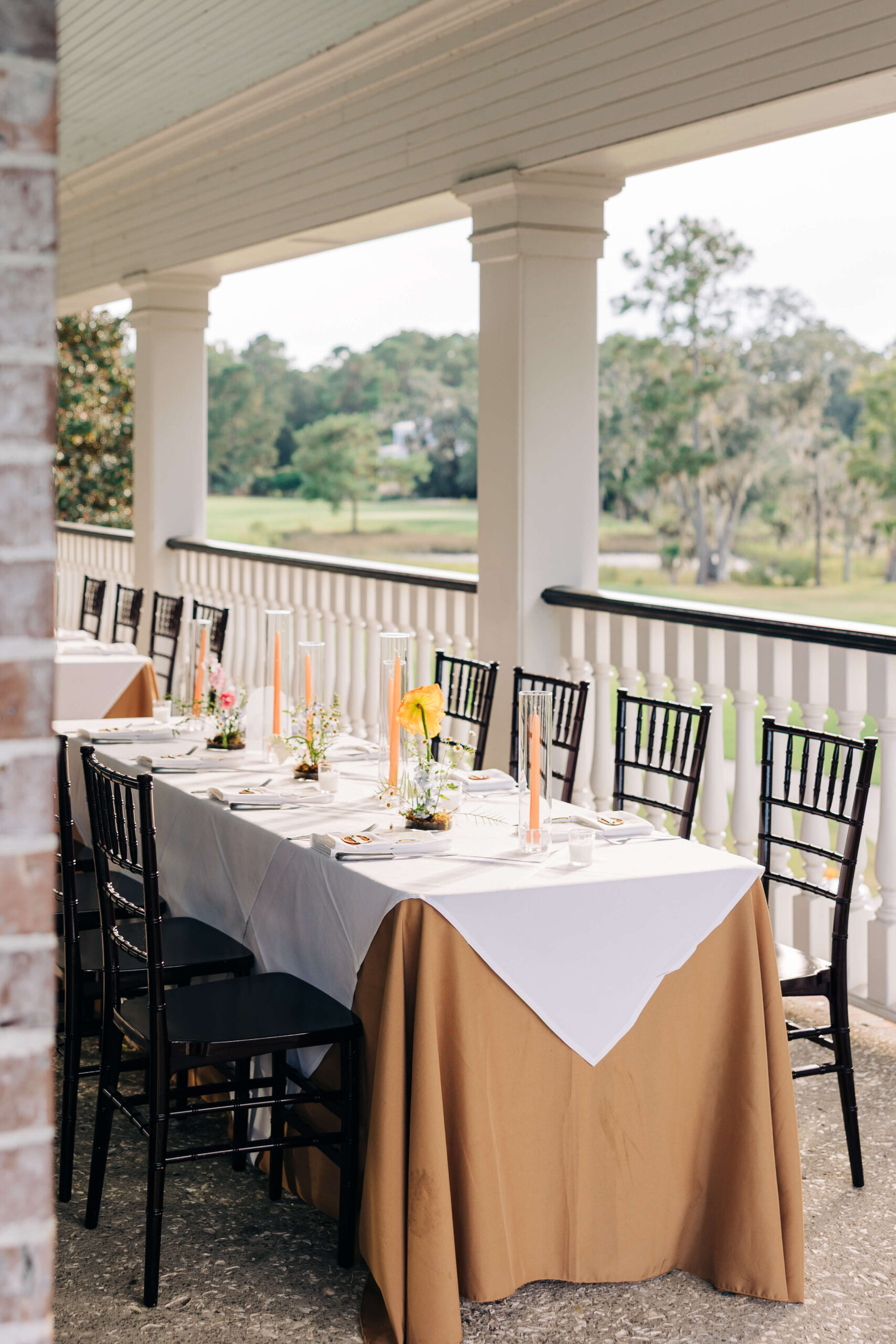 Details of a long Dunes West Golf Club wedding reception table set up on the porch with black chairs