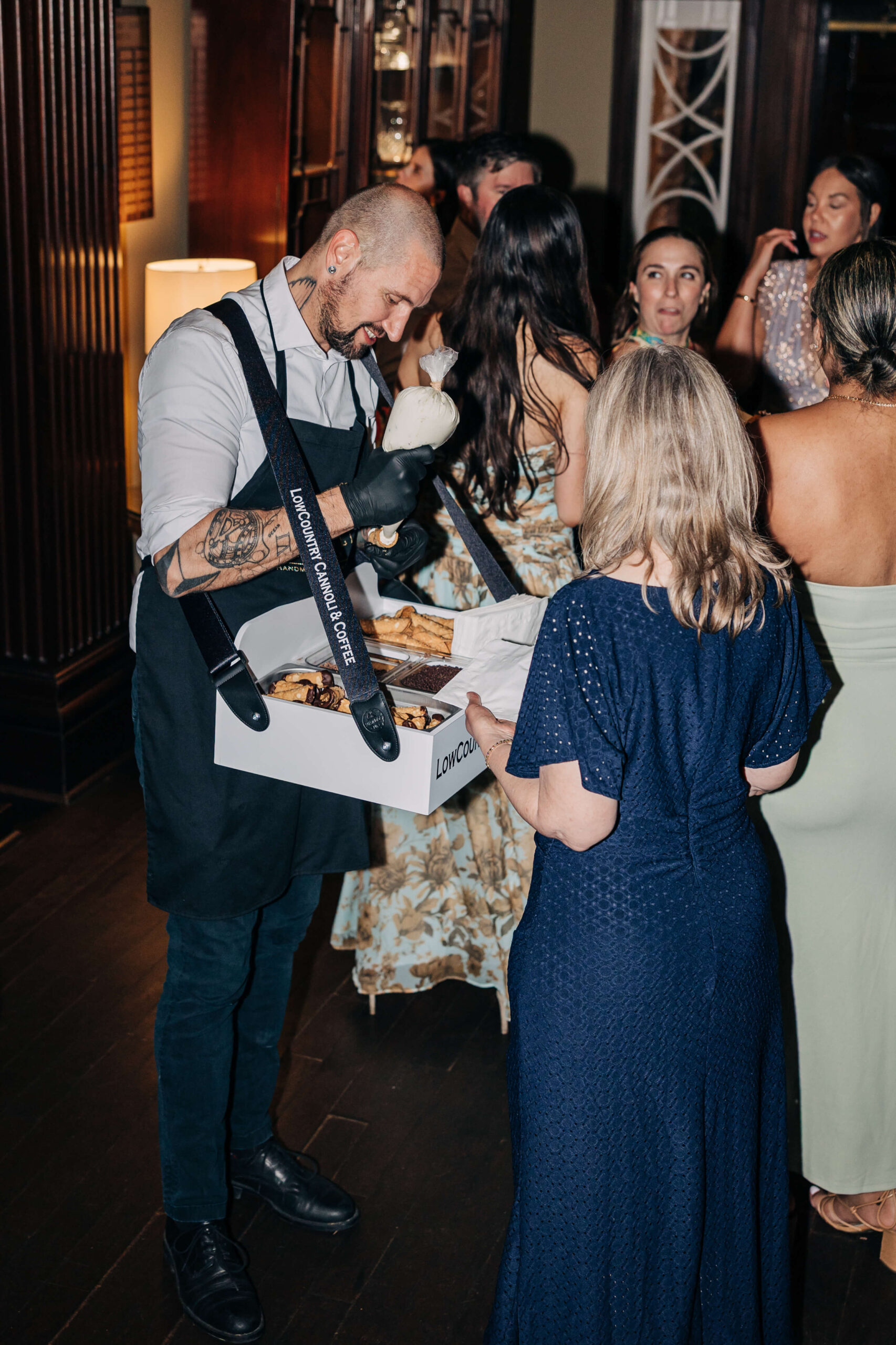 A woman in a blue dress picks deserts from a waiter with a tray