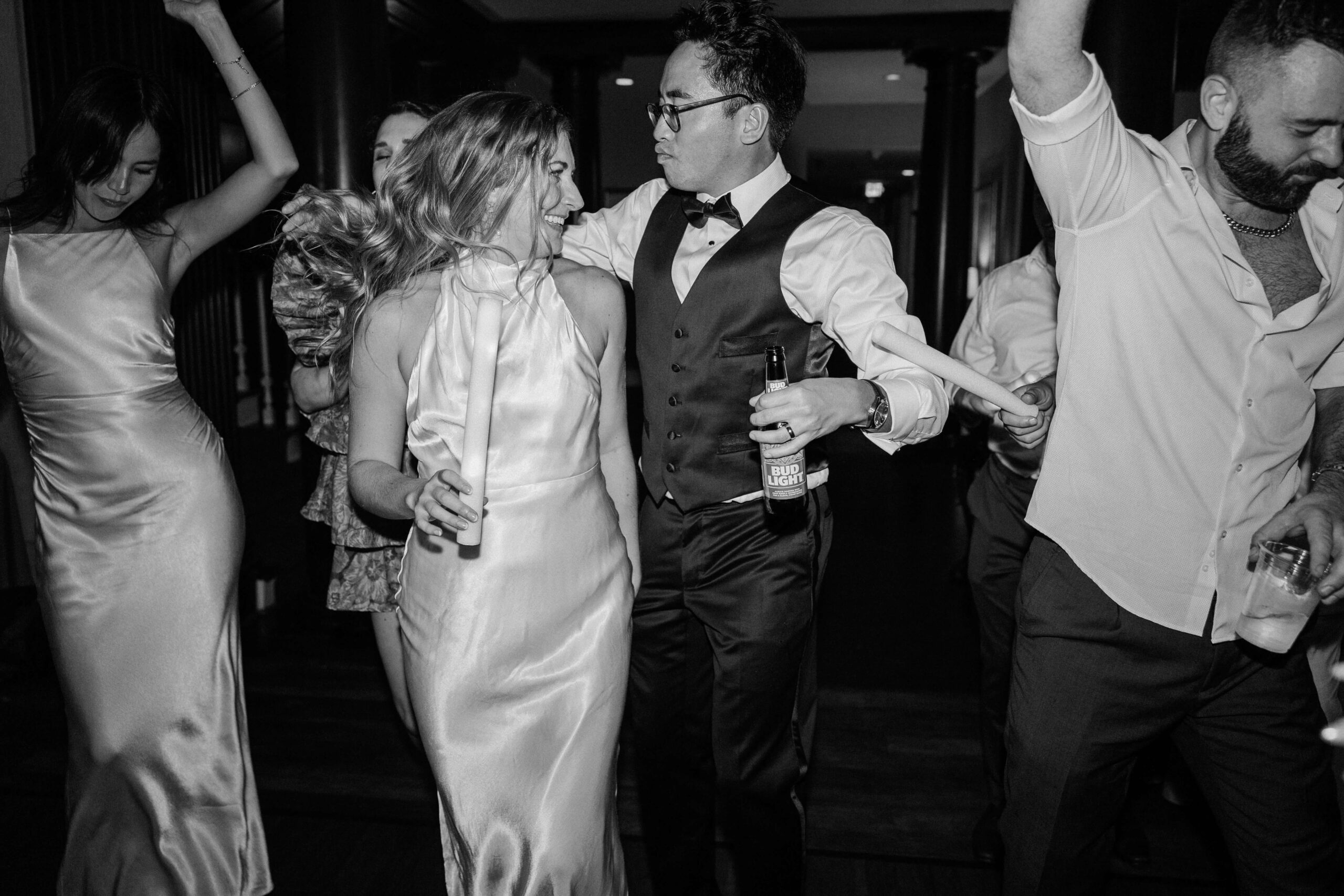 A bride and groom dance with their guests and light sticks during their reception