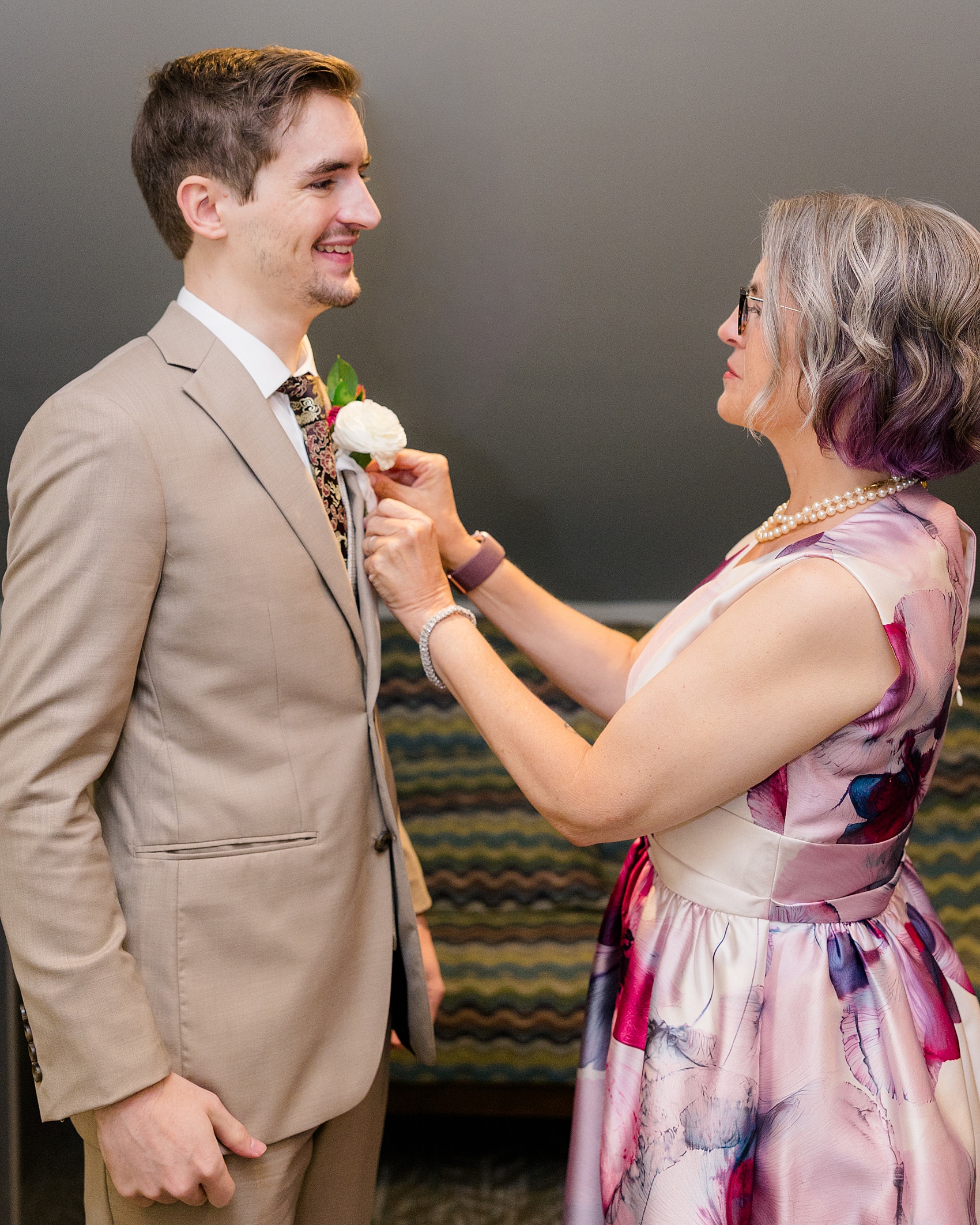 Mom in a purple dress helps groom put on boutonniere