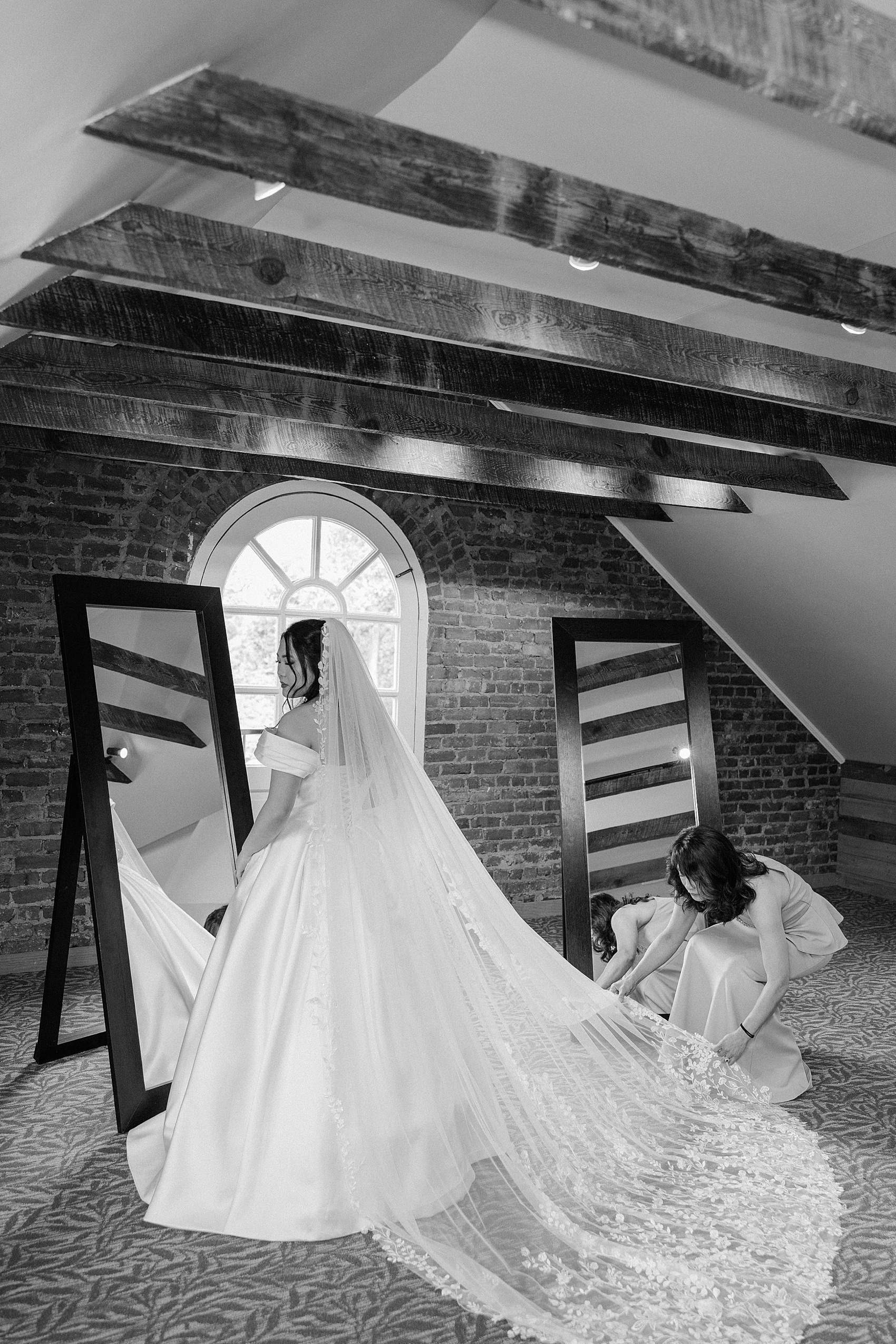 A bride looks over her shoulder while getting ready with long veil handled by bridesmaid