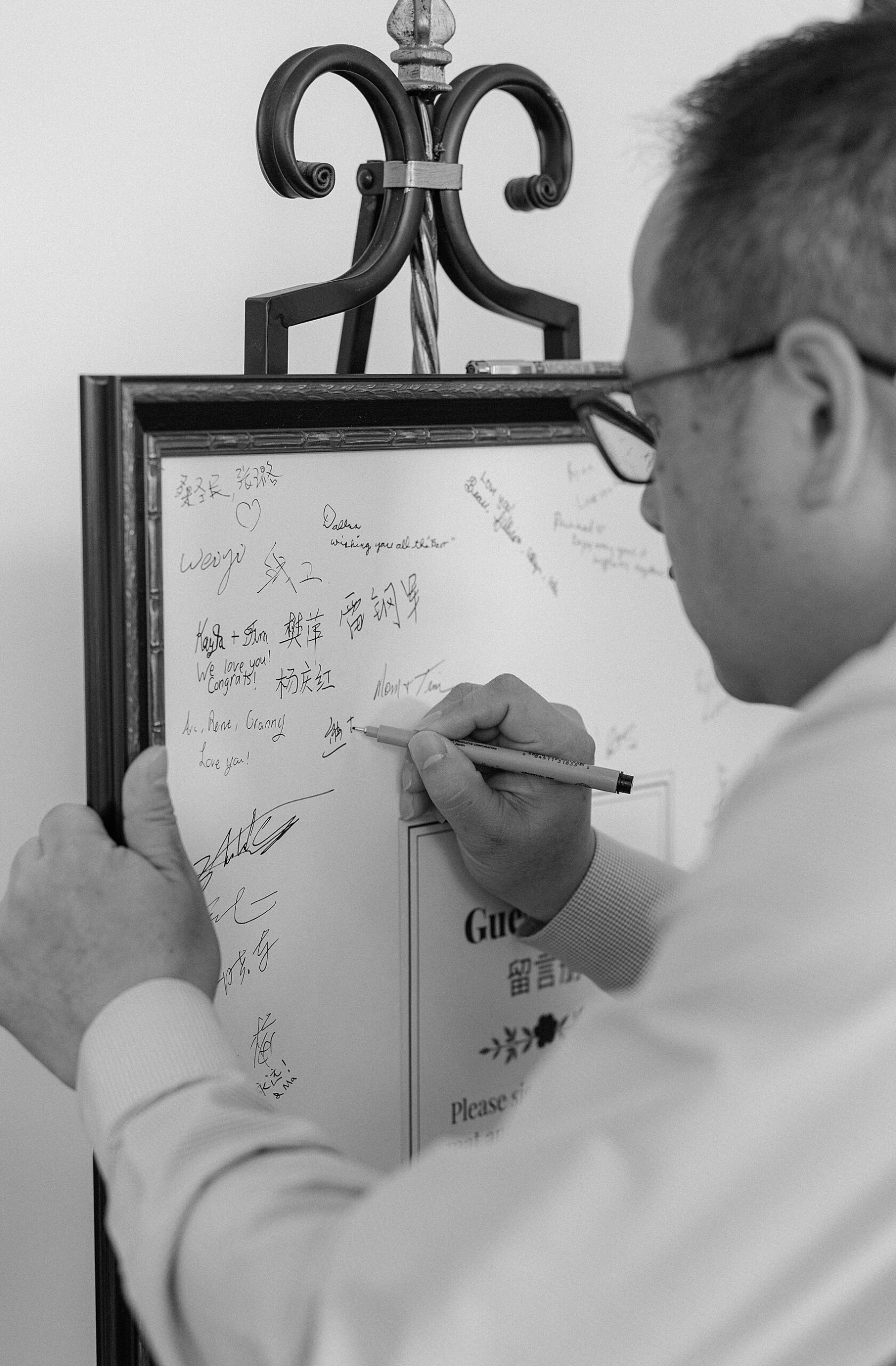 A man signs a guestbook in a frame on a stand in black and white