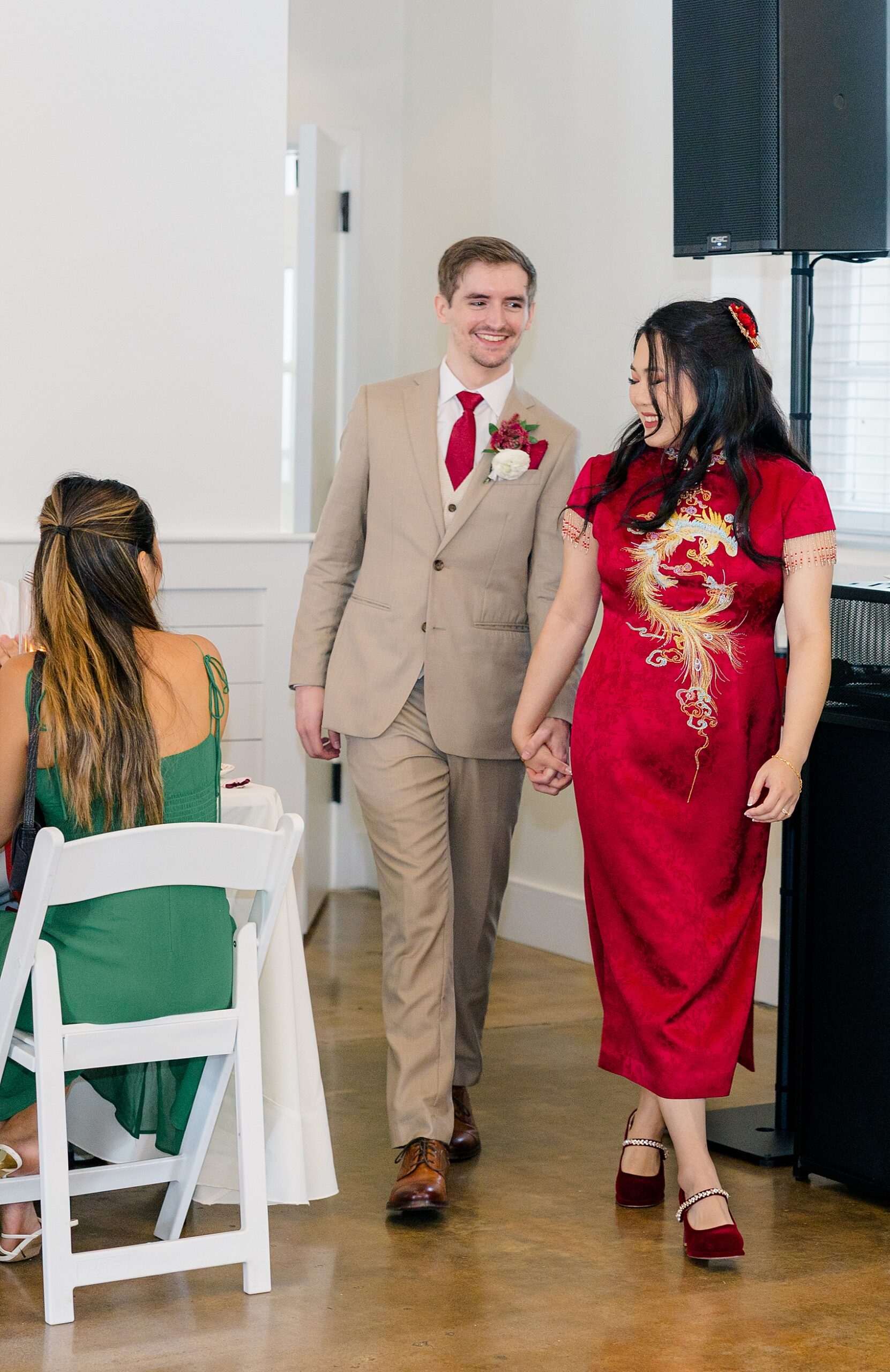 A bride in red walks her groom into their reception holding hands at the barn at reynolda village wedding venue