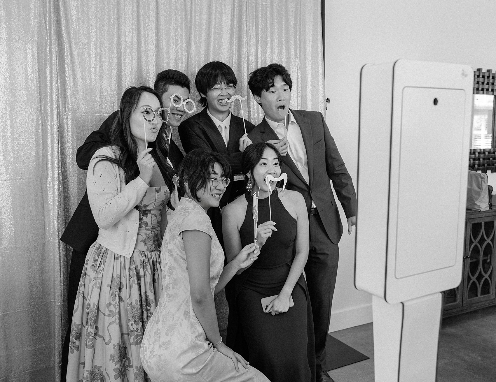 A group of friends play with props in a black and white photo of them in a photo booth
