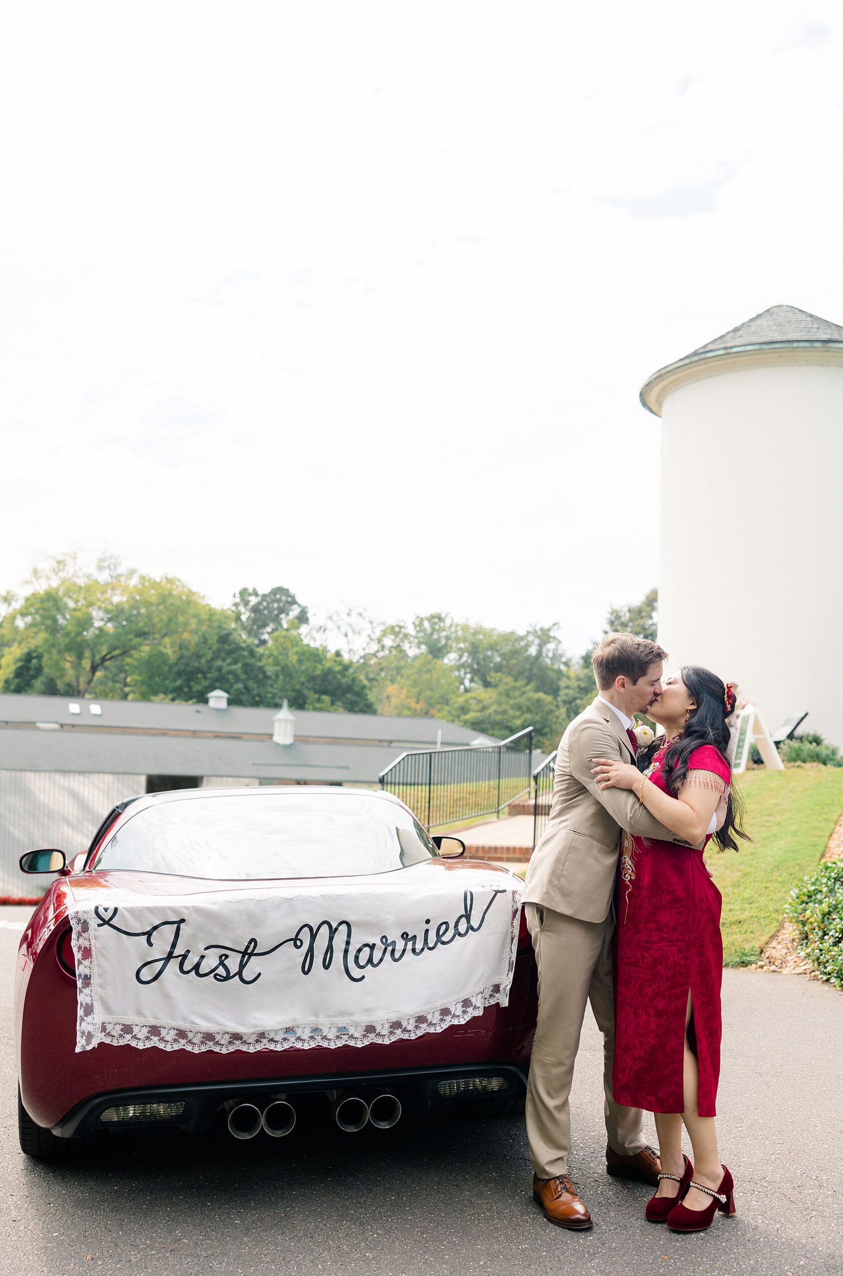 Newlyweds kiss behind a red corvette at the barn at reynolda village wedding venue with just married blanket