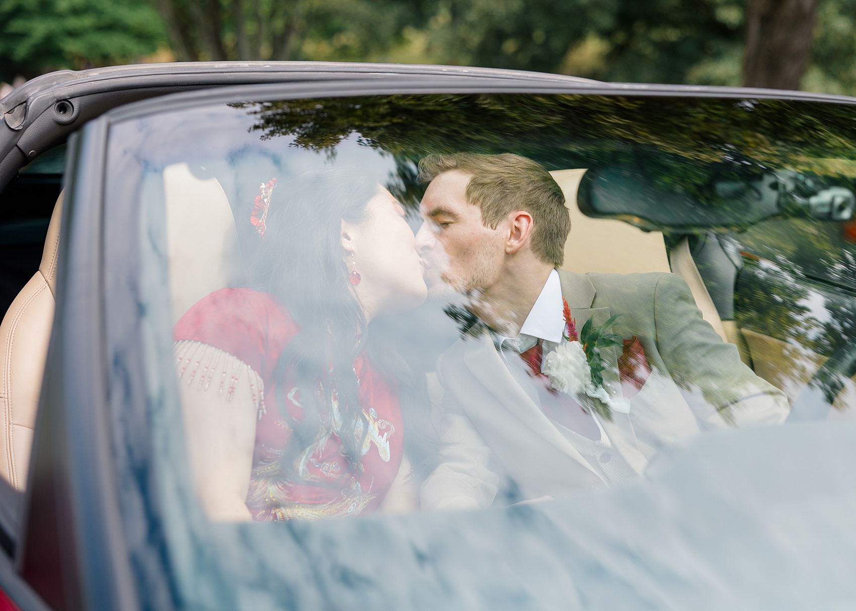 A bride and groom kiss in a convertable