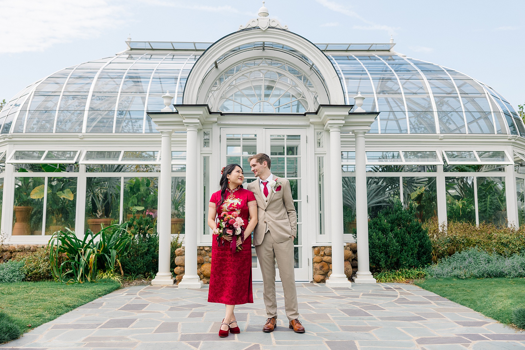 Happy newlyweds smile at each other in front of greenhouse doors in red and tan at the barn at reynolda village wedding venue
